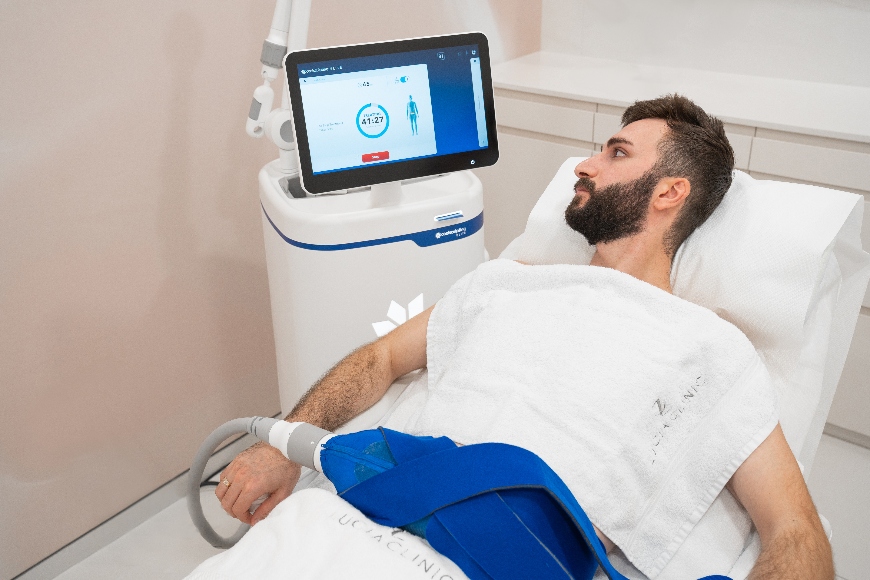 A person lies on a treatment bed, connected to a medical device with a touchscreen displaying a countdown timer and health stats.