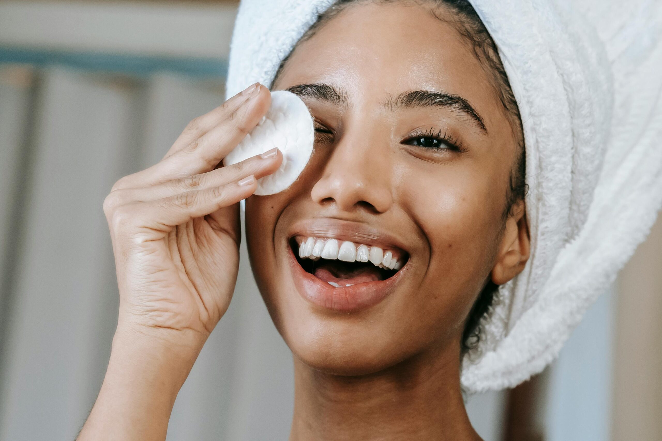 Ethnic smiling woman wiping face with cotton pad