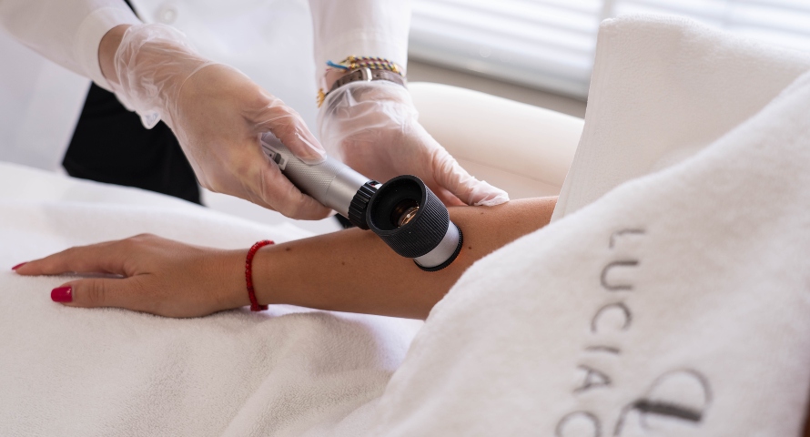 Dermatologist using a dermatoscope to examine a mole on a patient’s arm at Lucia Clinic.