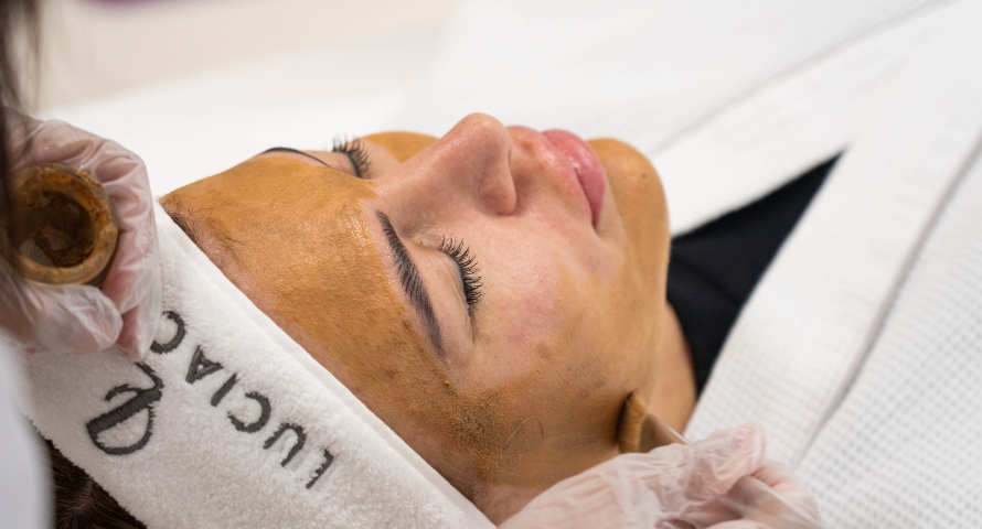 Woman receiving a facial treatment with a golden-brown mask applied.