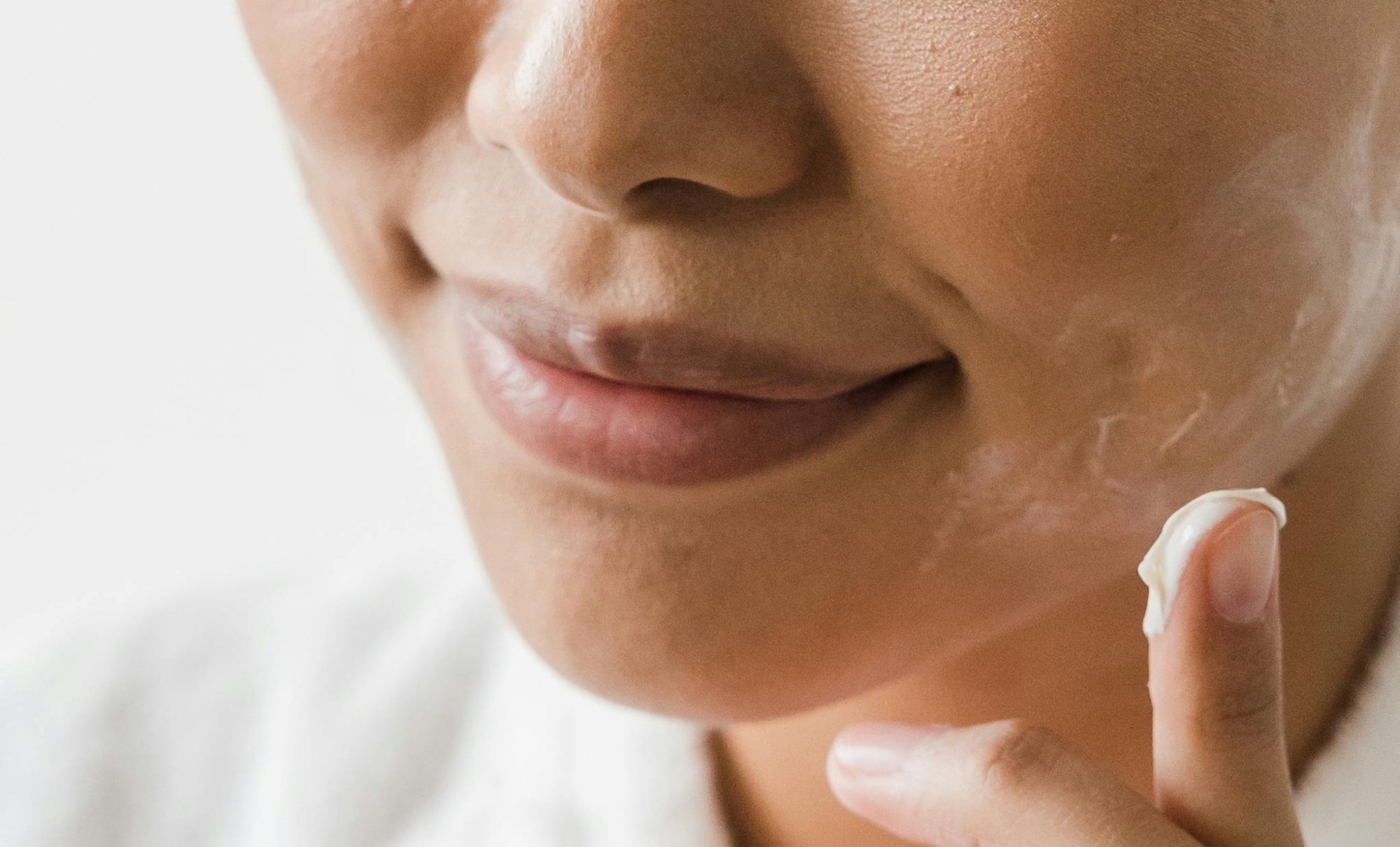 A close-up of a woman's face as she applies cream.