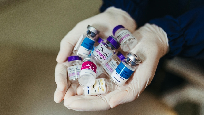 A doctor in white gloves holding a lot of empty botox vials