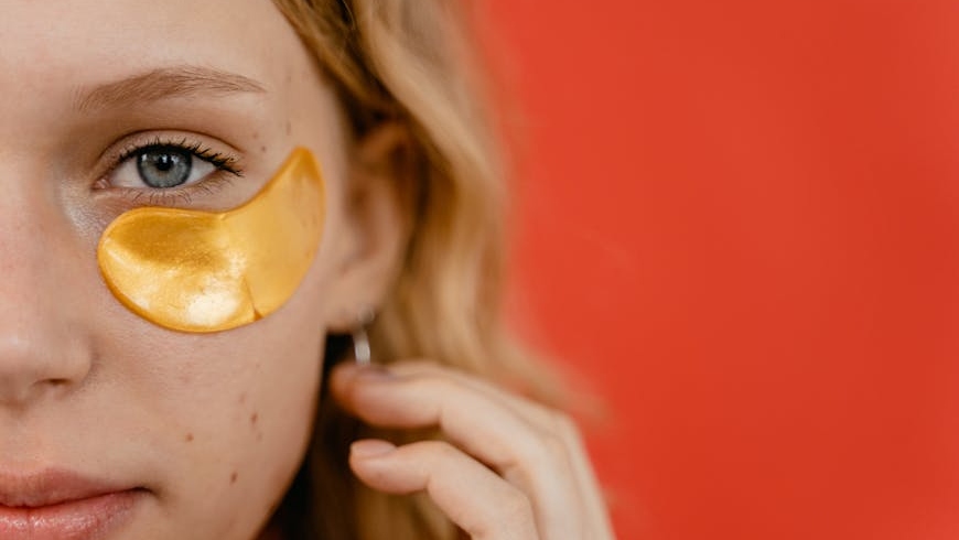 Half of a face of a woman doing her skincare as the first step of her dark circles under eyes treatment with gold undereye patches.