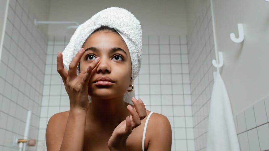 A woman with a white towel on her head applying a face cream