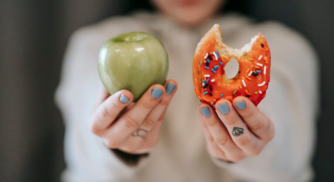 a woman holding a doughnut in one hand and an apple in the other 