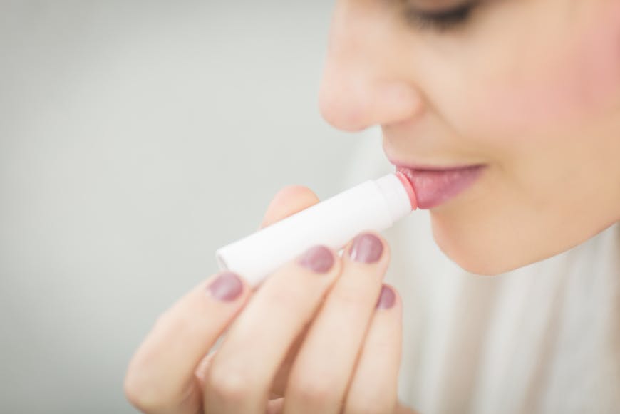 A woman putting lip balm after learning about dos and don'ts after lip fillers