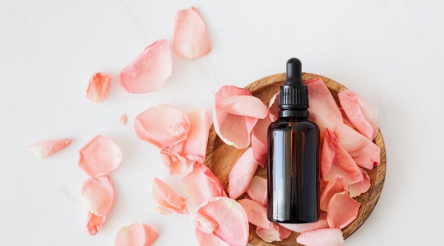 a serum and rose petals on a white surface 