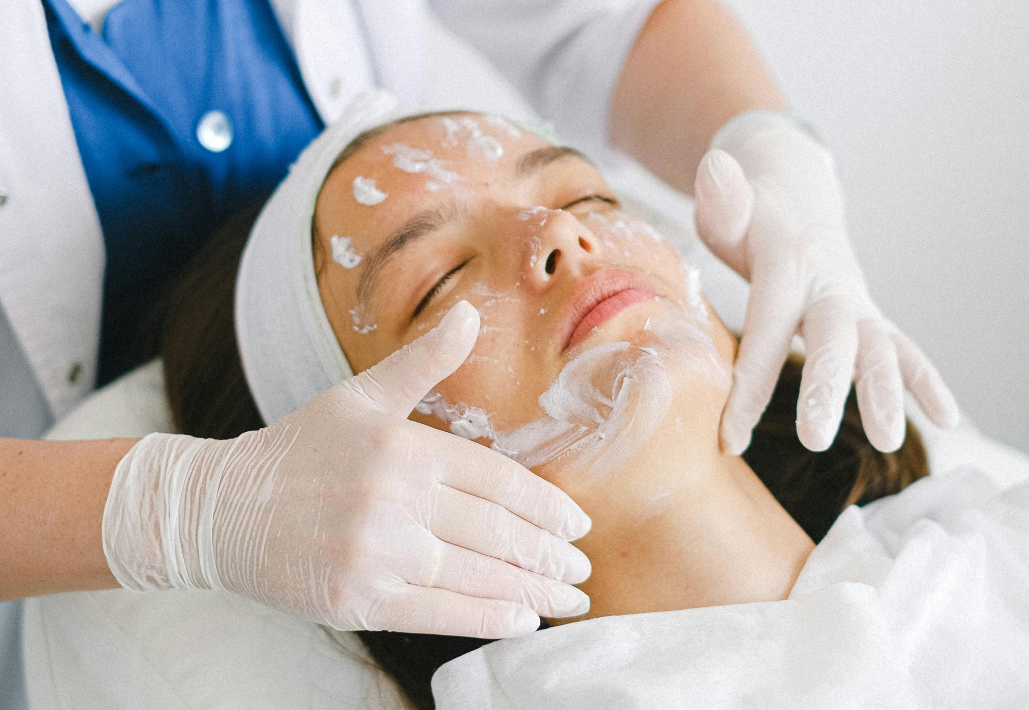 Cosmetologist applying facial mask on customer face in spa salon