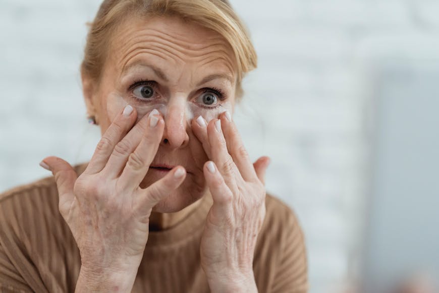 An older woman applying a cream on her face.