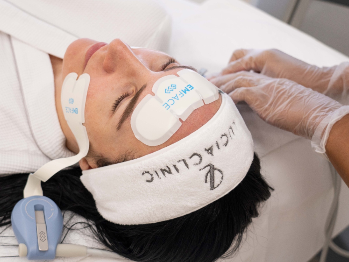 A person receiving a facial treatment, wearing a headband with "Clinic" embroidered, while a gloved hand performs the procedure.