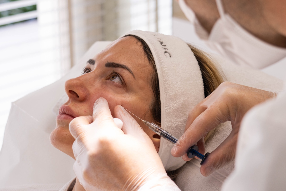 A cosmetologist administers an injection during a skincare treatment in a bright, serene room with natural light.